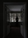 Back view of unrecognizable woman standing near large window in dark room in house in daytime