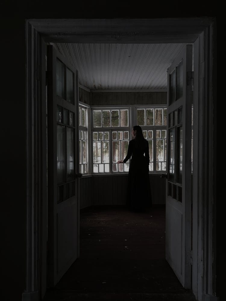 Pensive Female Standing Near Window In Dark Room