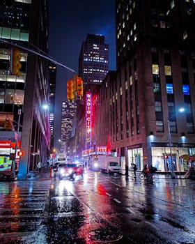 Vibrant night street scene of Radio City Music Hall in New York City with reflections on wet pavement.