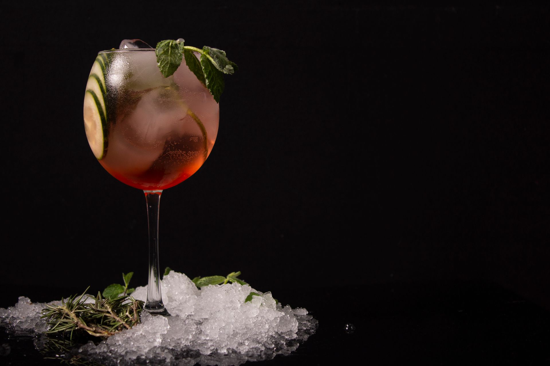 Chilled cocktail with cucumber and mint, served in a glass with ice against a dark background.