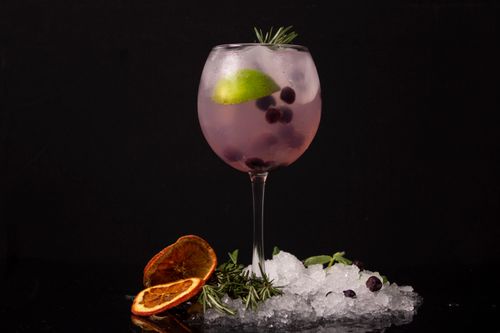 Free A stylish pink cocktail garnished with lime, berries, orange slices, and rosemary on a dark background. Stock Photo