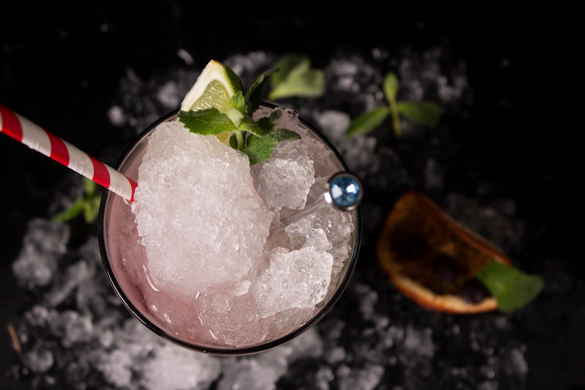 Overhead view of an iced drink with mint, lime, and a striped straw.
