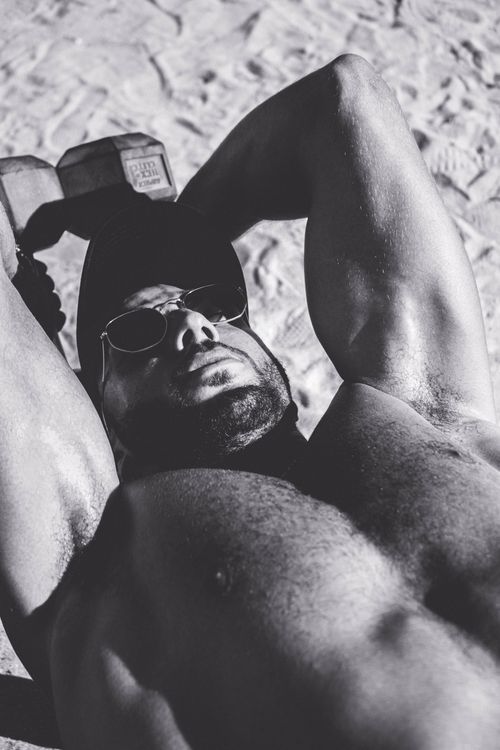 Free Grayscale image of a muscular man sunbathing on sand while exercising. Stock Photo