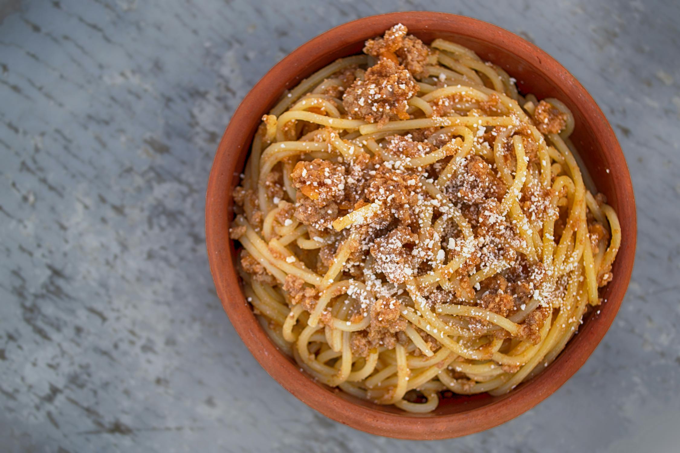 bowl of spaghetti covered in parmesan cheese on grey countertop