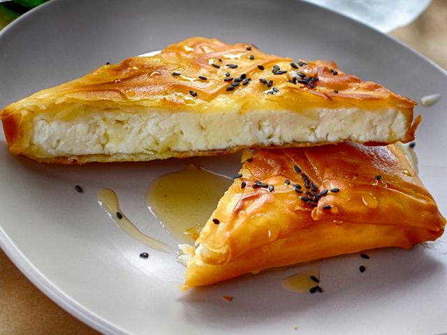 A delicious Greek cheese pie drizzled with honey, garnished with sesame seeds on a plate.