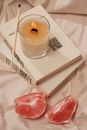 High angle of burning aroma candle with incense stick on books near pieces of ripe grapefruit on creased fabric