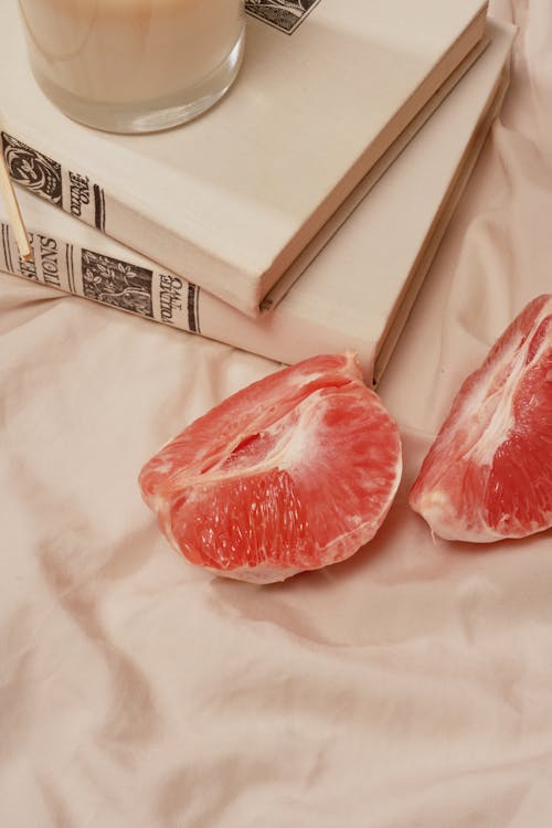 Ripe grapefruit placed near books and candle