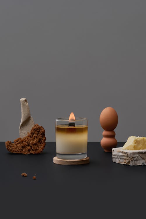 Composition of burning aroma candle placed near decorative art objects on gray background