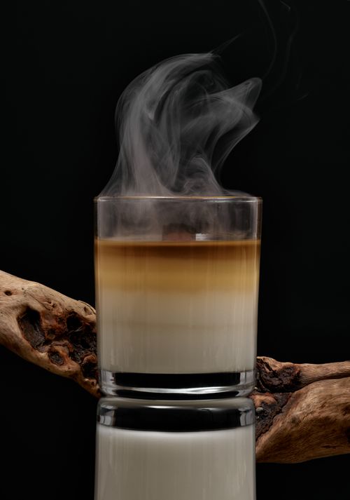 Free Aromatic transparent glass holder with wax candle with smoke near driftwood on black background Stock Photo