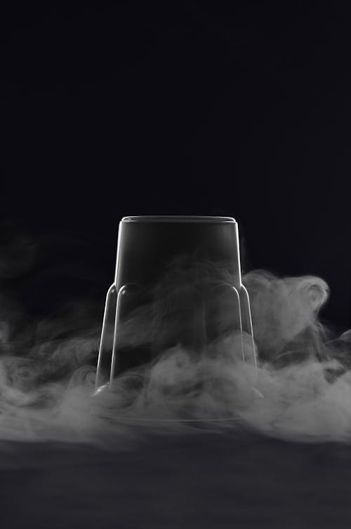 Transparent inverted glass cup with cloud of steam against black background in studio