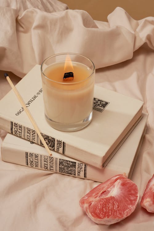 Burning candle on books near grapefruit on creased cloth