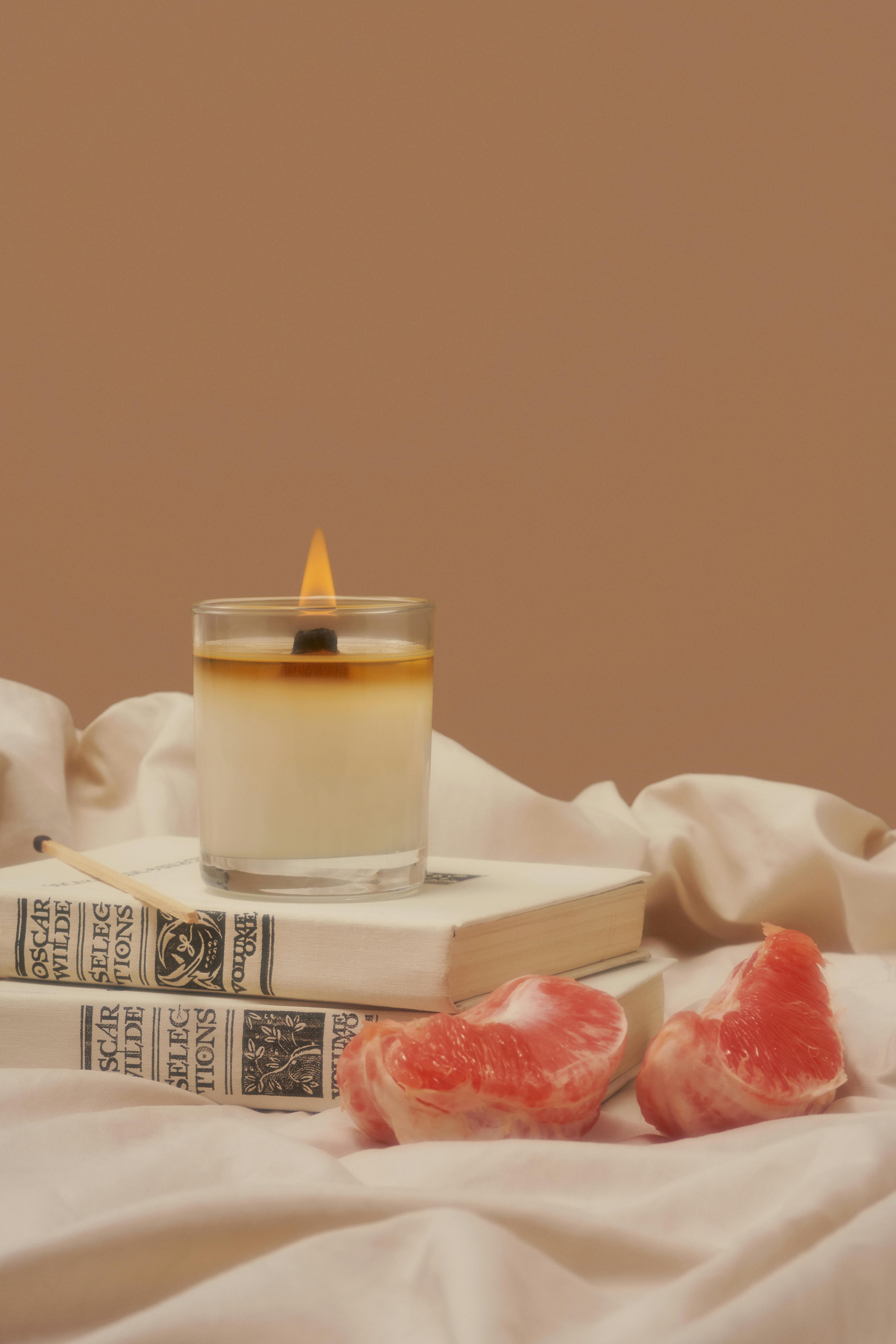 burning aroma candle on books near grapefruit
