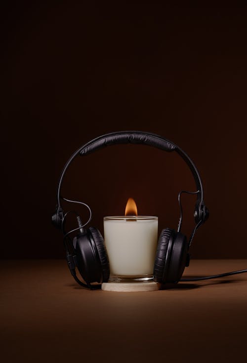 Burning wax candle with headphones for listening relax music and aromatherapy session against brown background