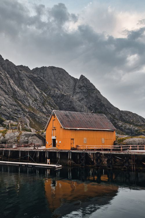 Free Rustic yellow boathouse by the water with mountain view in Nordland, Norway. Stock Photo