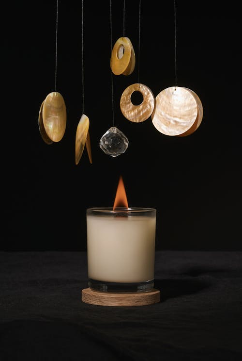 Burning aroma candle placed under round shaped hanging decor against dark black background