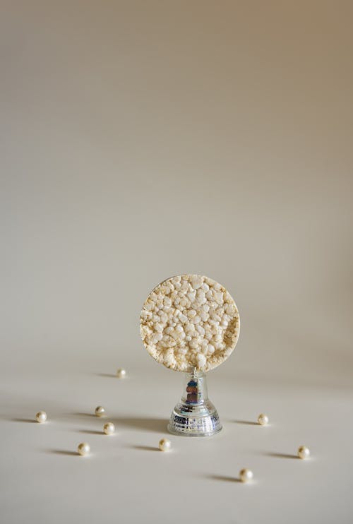 Composition of puffed rice cake on metallic stand around small pearls in white studio