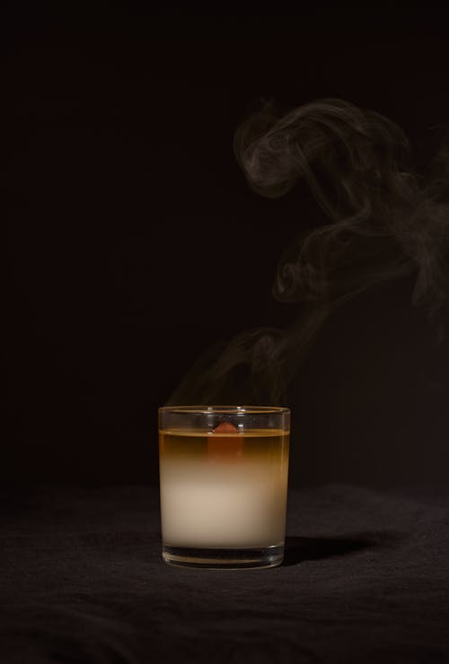 Wax aroma candle in transparent glass holder with smoke placed against black background