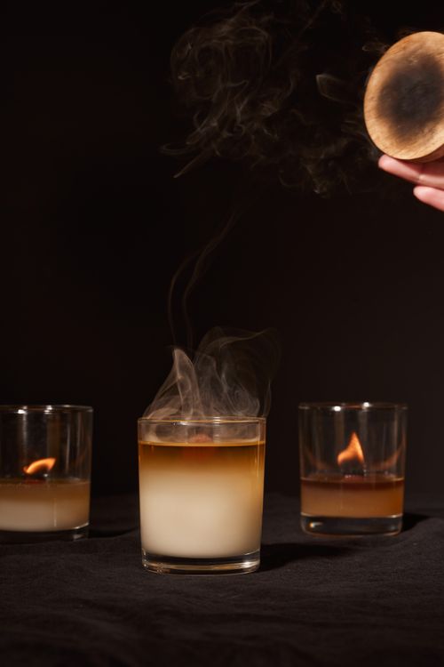 Free Crop anonymous person extinguishing fragrant wax candle with fume against black background in studio Stock Photo