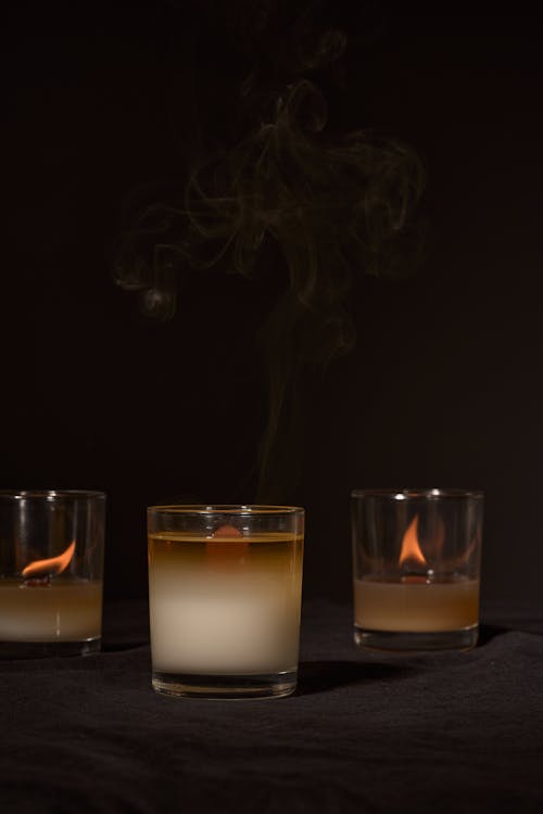 Burning aromatic candles with burning blazes placed near smoking in glass holders on black background