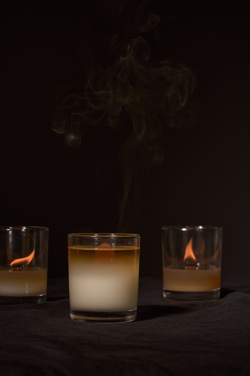 Free Burning aromatic candles with burning blazes placed near smoking in glass holders on black background Stock Photo