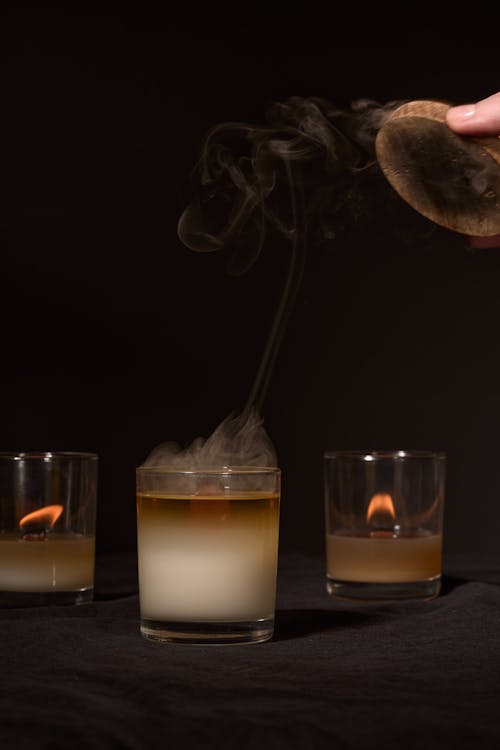 Crop anonymous person extinguishing flame of aroma candle placed against black background in studio