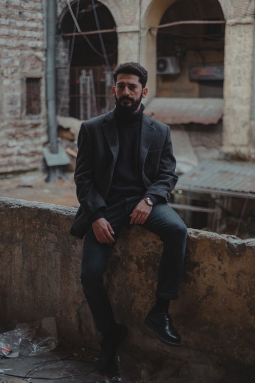 Free Full body of masculine ethnic male in stylish outfit looking at camera while sitting in destructed house with concrete ruins Stock Photo