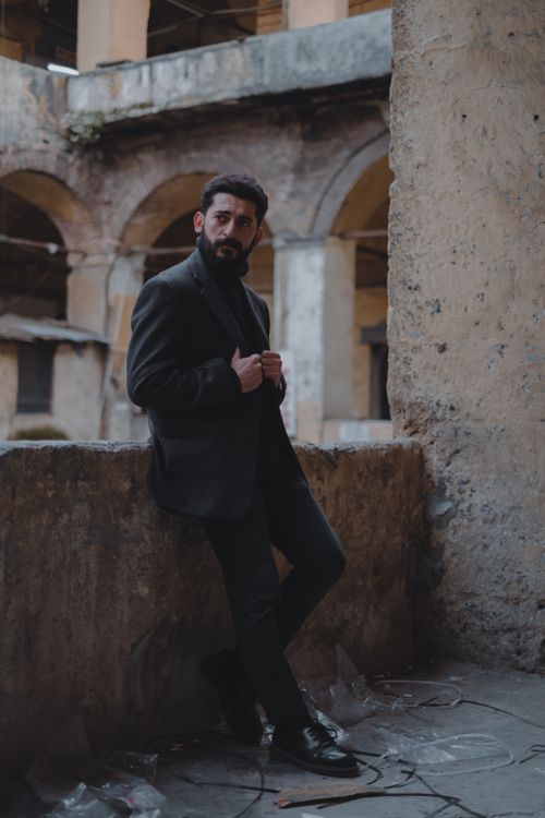 Free Full body of ethnic male in black suit and jeans standing at balcony fence of aged building with patio and looking away Stock Photo