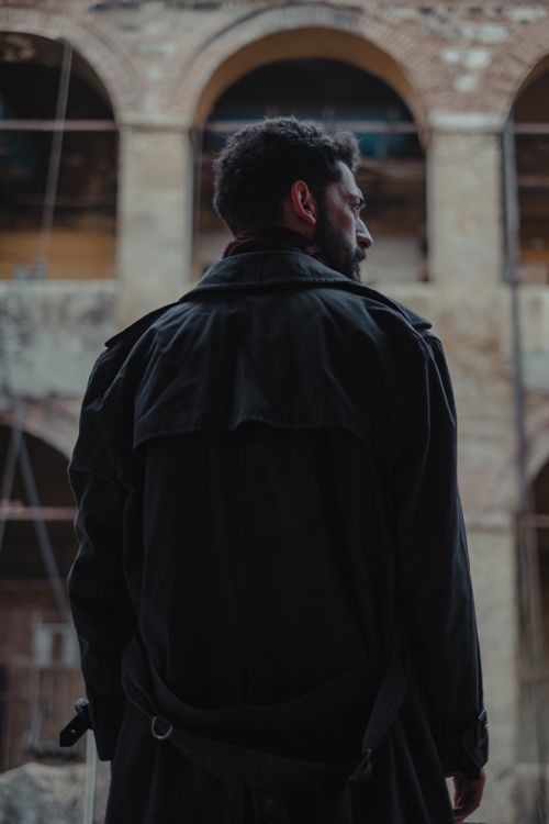 Free Back view of male in dark coat standing near old building and looking away against blurred background Stock Photo