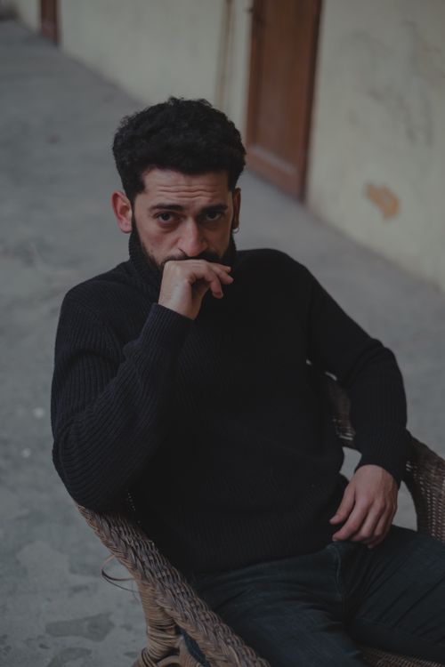 Free Pensive male touching lips while sitting on chair and looking at camera in shabby corridor against blurred background Stock Photo