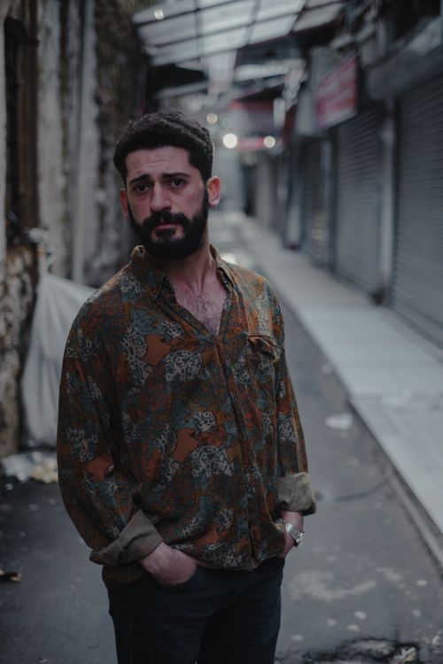 Free Thoughtful bearded male looking away while standing with hands in pockets on backstreet near building on blurred background Stock Photo