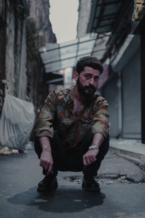 Free Serious man in casual clothes and sitting on shabby asphalt and looking away on backstreet Stock Photo