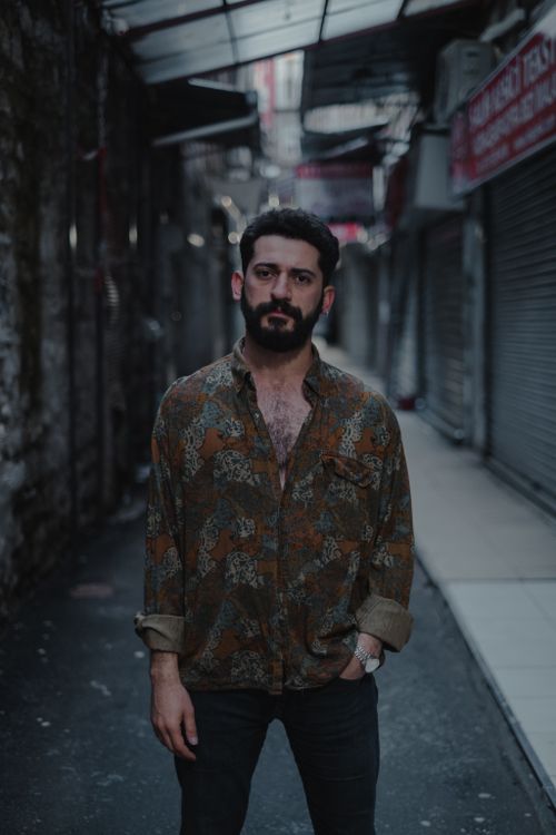Free Unshaven emotionless ethnic male looking at camera while standing on street near shabby building Stock Photo