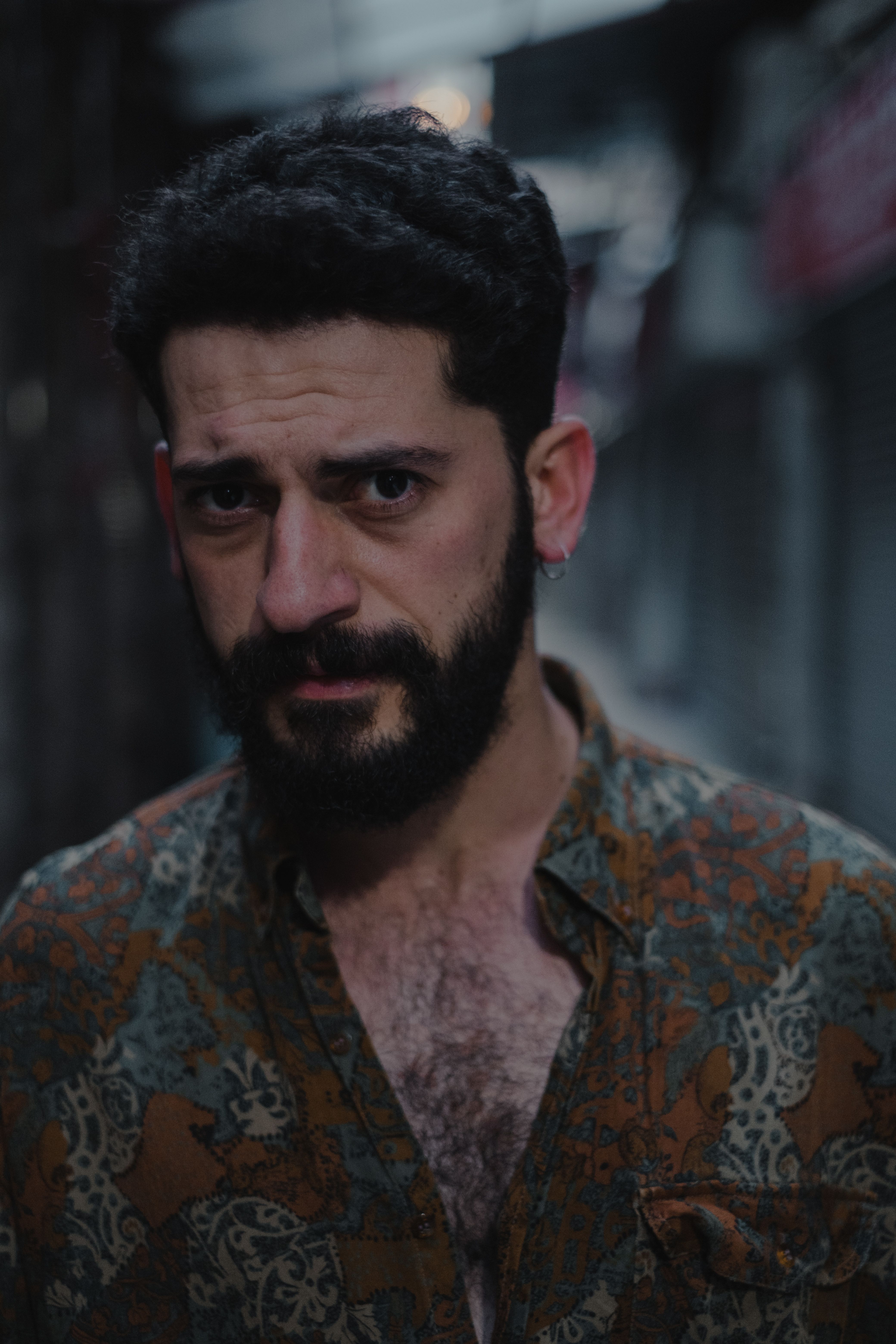 Portrait of ethnic serious bearded brunet in t shirt looking at camera against blurred background