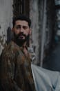 Worried ethnic male with beard looking away while leaning on street near shabby wall