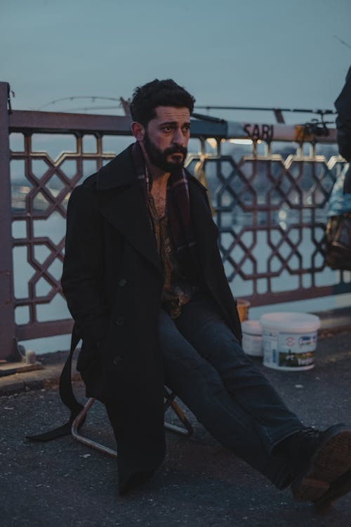 Man in black coat sitting on embankment in dusk