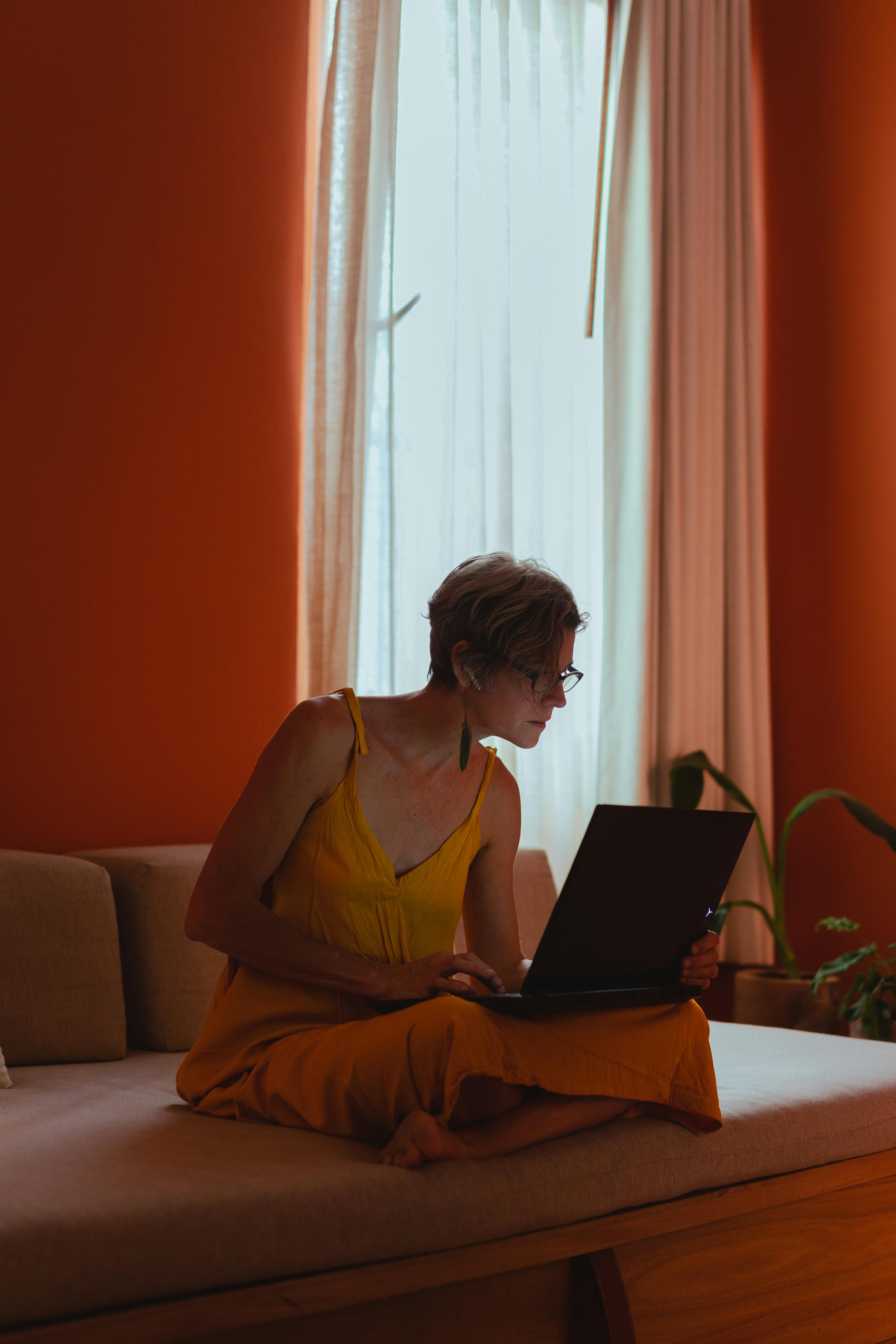 Elderly woman sitting and working on laptop in a bright room, embracing modern technology.