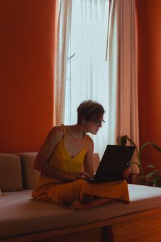 Elderly woman sitting and working on laptop in a bright room, embracing modern technology.