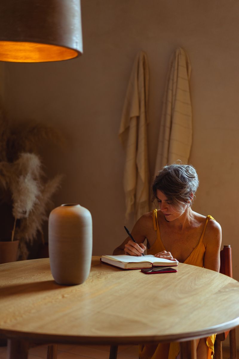 Person recording thoughts in a journal near a window; illustrative stock photograph