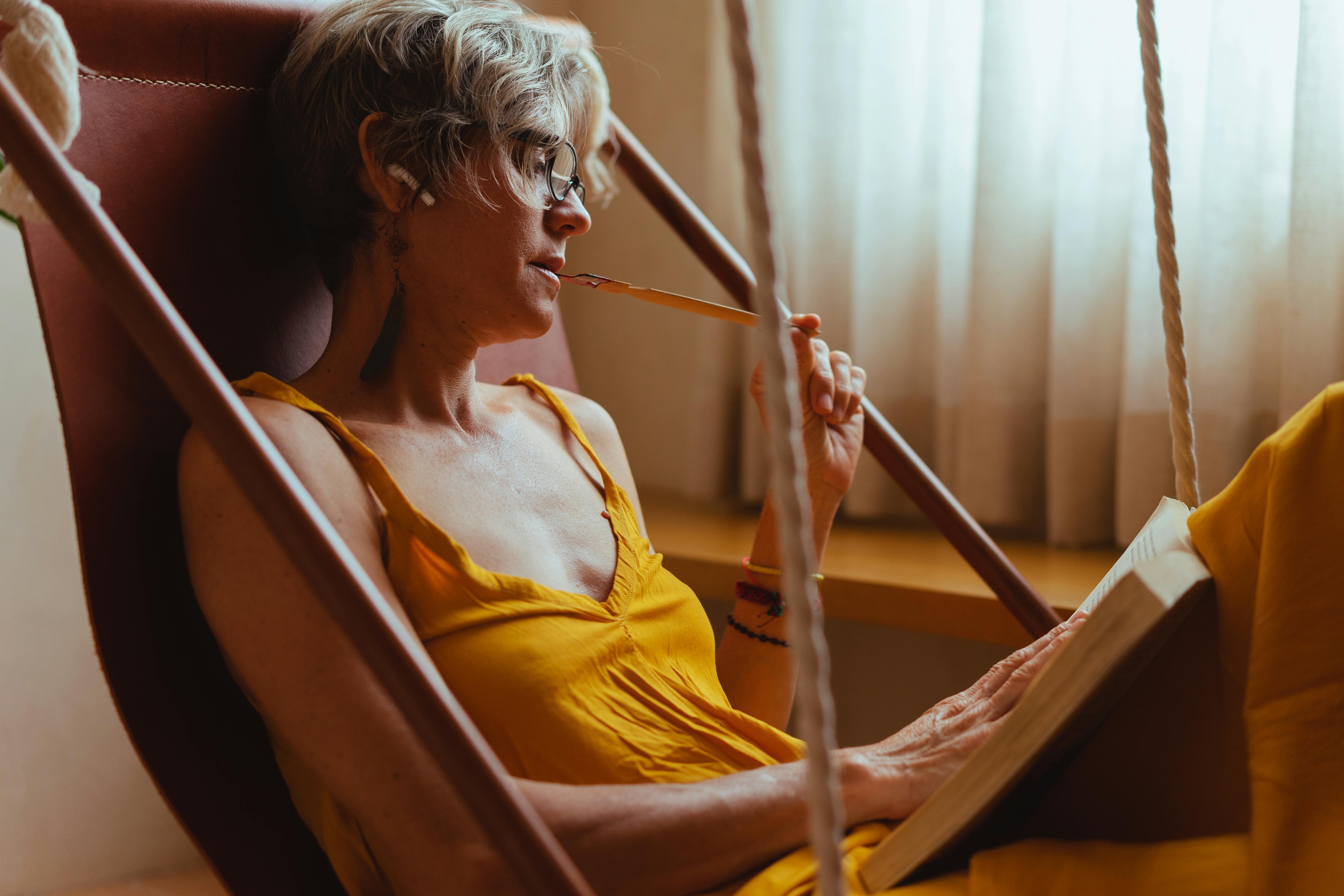 Young person reading a book in a sunlit hammock, looking relaxed and content