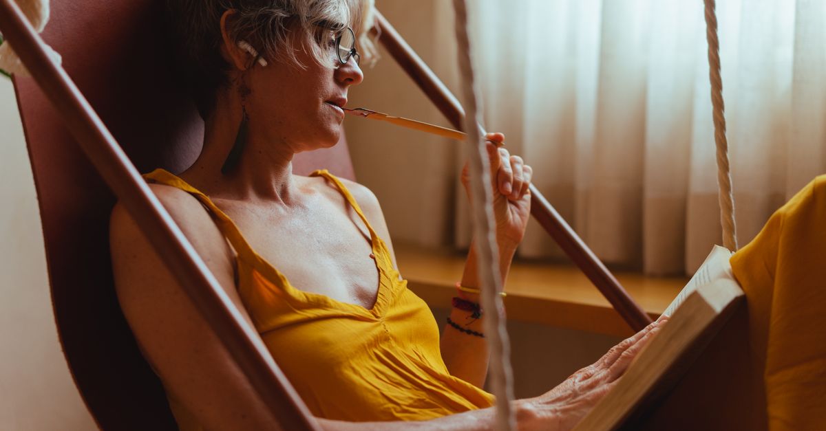 Young person reading a book in a sunlit hammock, looking relaxed and content