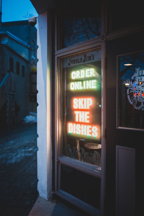 Luminous neon signboard asking ordering online and hanging on window of night cafe in evening
