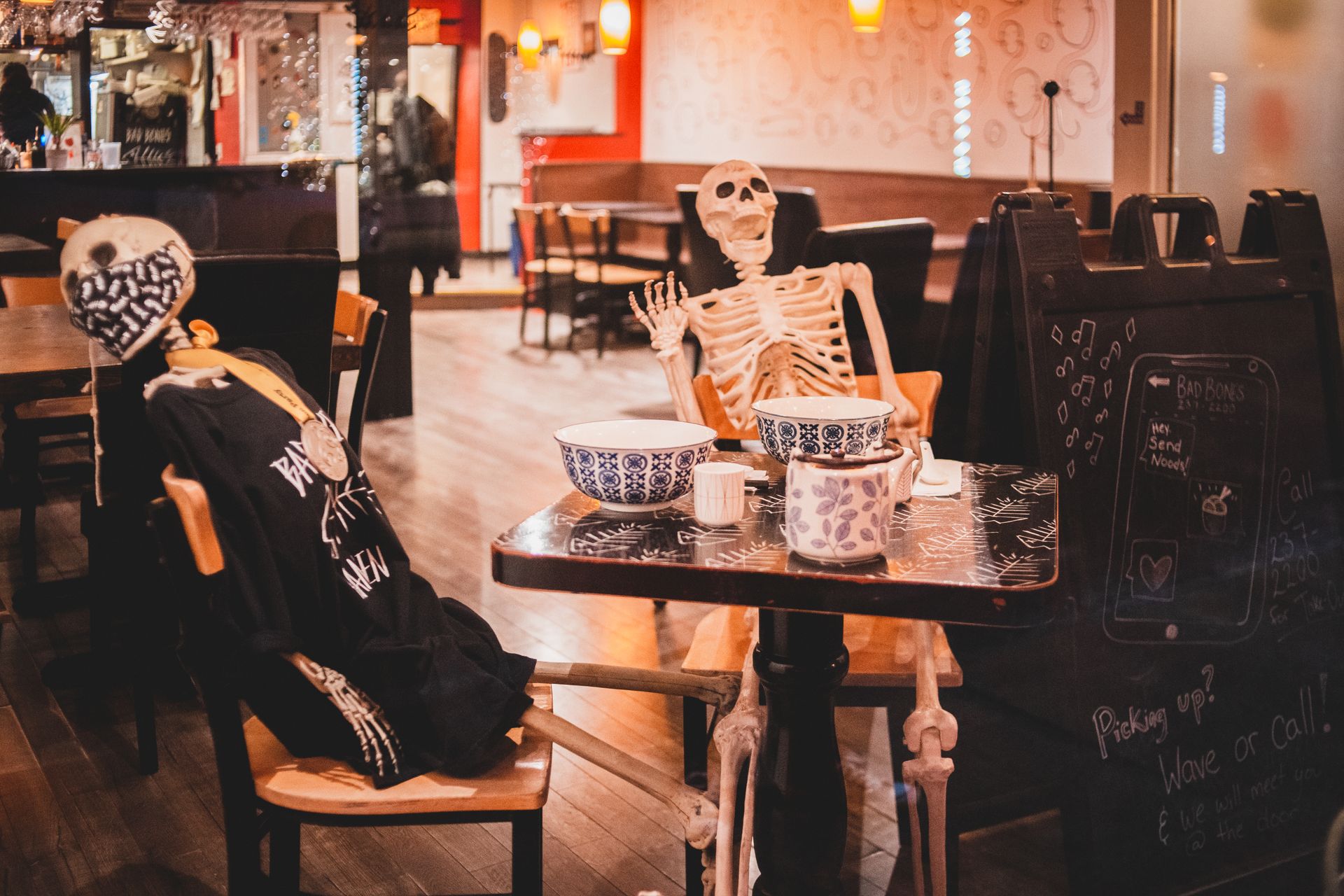 Modern cozy cafe interior with skeletons at table as decoration for Halloween holiday celebration