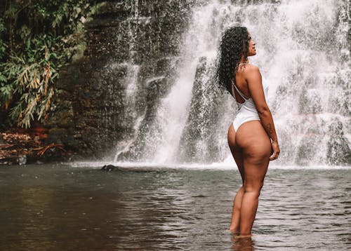 Black woman in swimsuit standing near waterfall