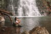 Free Full body side view of African American female in swimwear sitting on stone near rippling river and falling waterfall while admiring nature Stock Photo