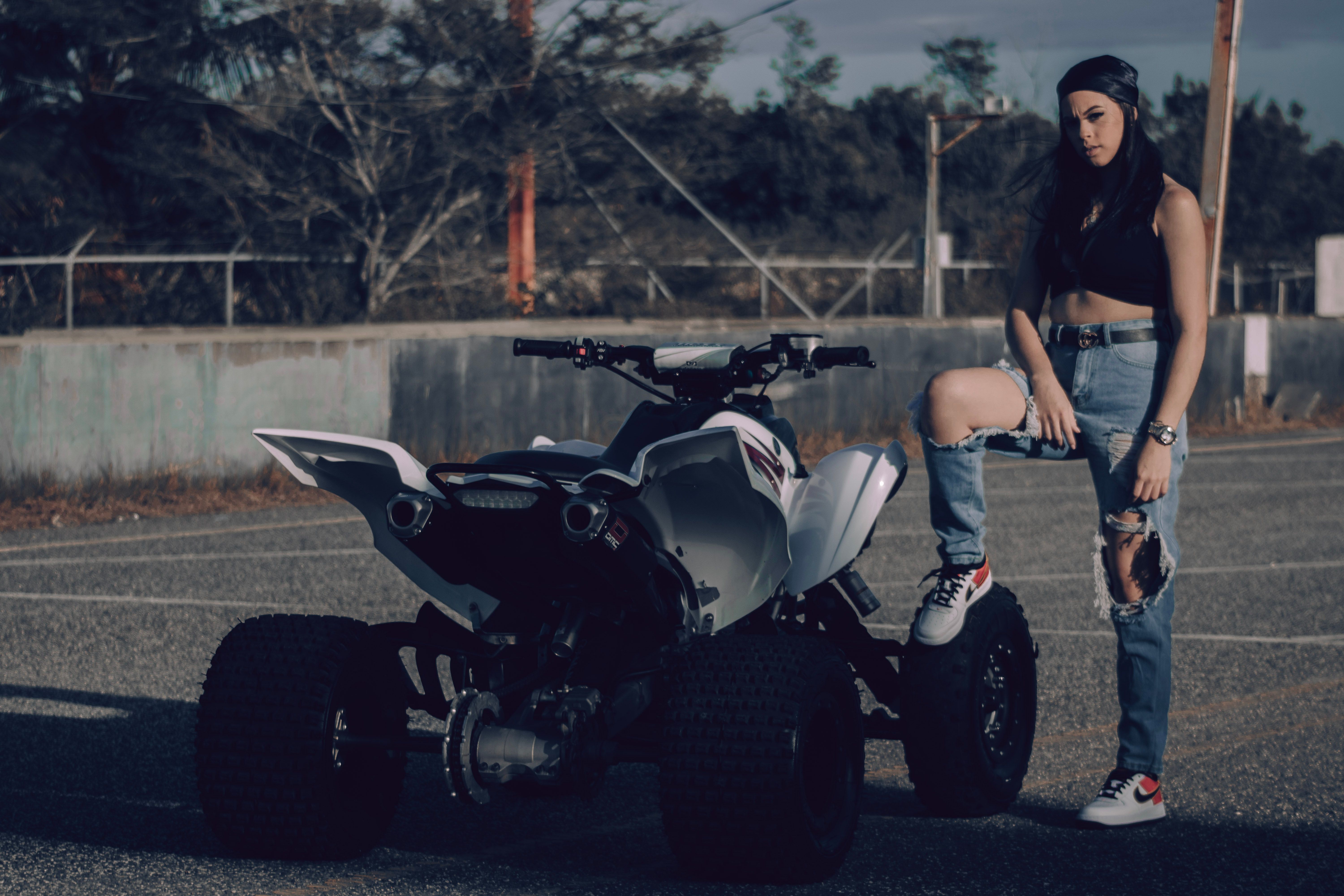 A stylish woman stands confidently beside an all-terrain vehicle outdoors.