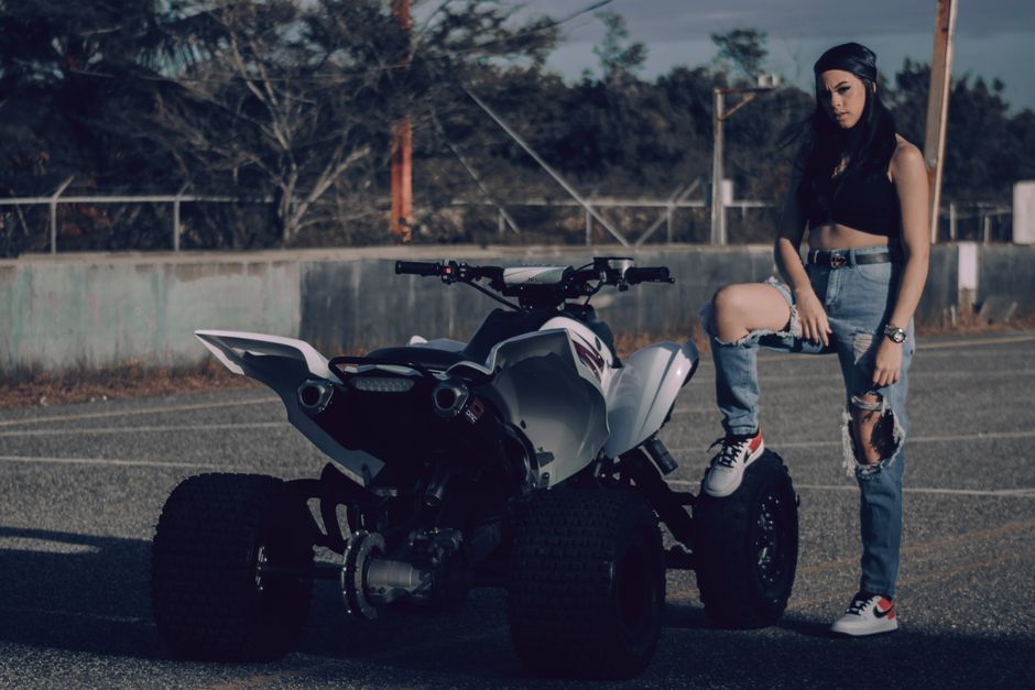 A stylish woman stands confidently beside an all-terrain vehicle outdoors.