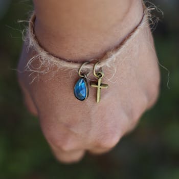Hand adorned with a bracelet featuring a blue teardrop gemstone and cross pendant in close-up.