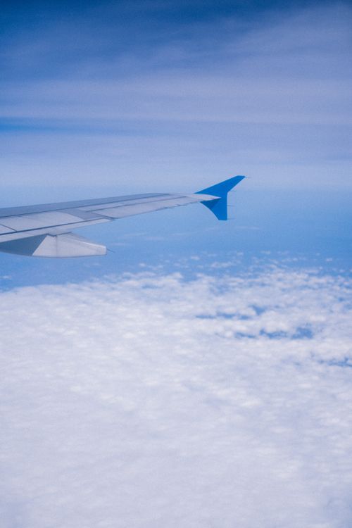 Free A serene view from an airplane showing its wing amidst fluffy white clouds and a clear blue sky. Stock Photo