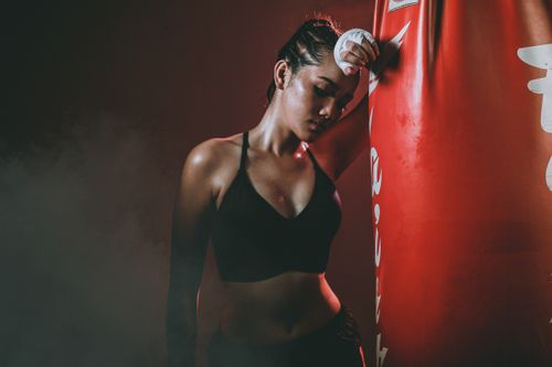 Free An athletic woman in a boxing gym taking a break beside a punching bag. Captured in moody lighting. Stock Photo