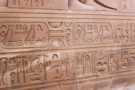 Detailed carvings of ancient Egyptian hieroglyphs on a stone temple wall in Aswan, Egypt.